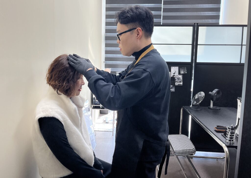 고객의 두피 상태를 직접 손으로 확인하며 수정과 사후관리를 상담하는 모습