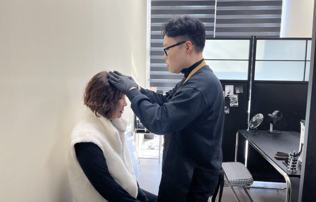 상담실에서 고객의 두상과 모발 흐름을 손으로 직접 살펴보는 상담 장면