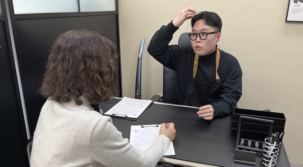 상담 테이블에서 두피문신 시술 범위와 그 이유를 설명하는 상담 장면